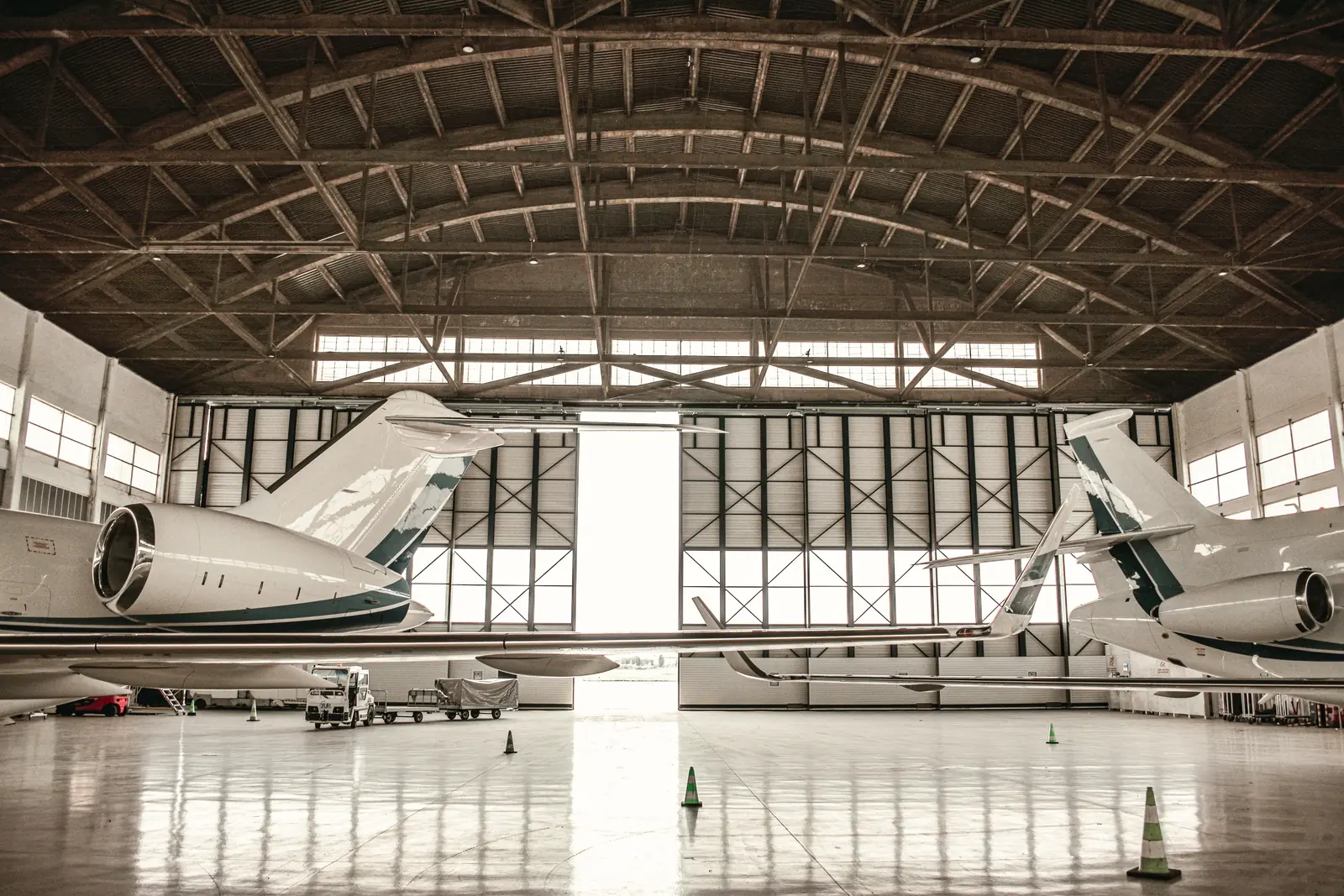 Business jets parked inside a large hangar in front of its tall doors